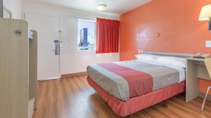 Quarto de hotel com cama, escrivaninha, janela com cortinas e porta.