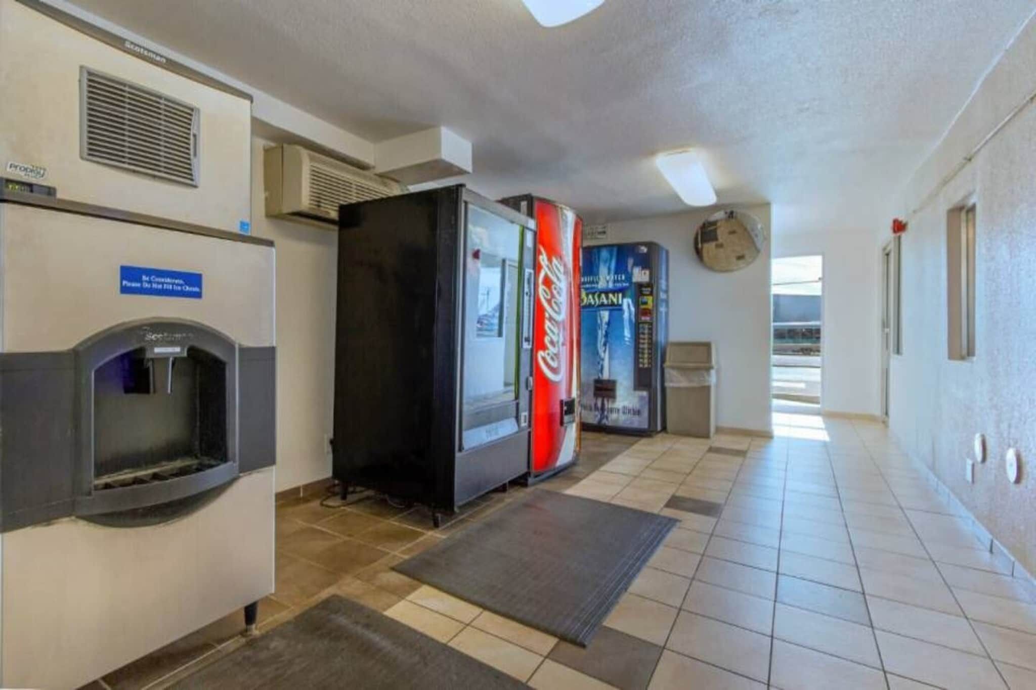 Un couloir avec des distributeurs automatiques, un point d’eau et un réfrigérateur rempli de Coca-Cola.