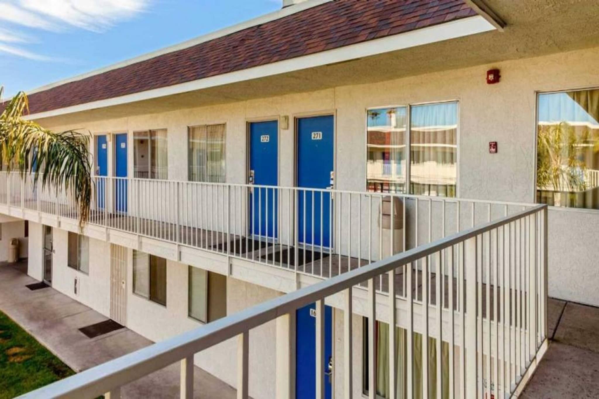 A multi-story motel with a flat roof, a covered outdoor area, and a series of blue doors.