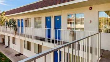 A multi-story motel with a flat roof, a covered outdoor area, and a series of blue doors.