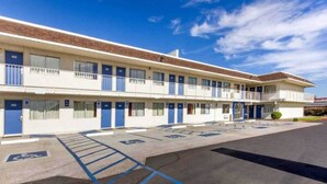 Un motel amb una zona de pàrquing, places de pàrquing adaptades i un cel blau clar.