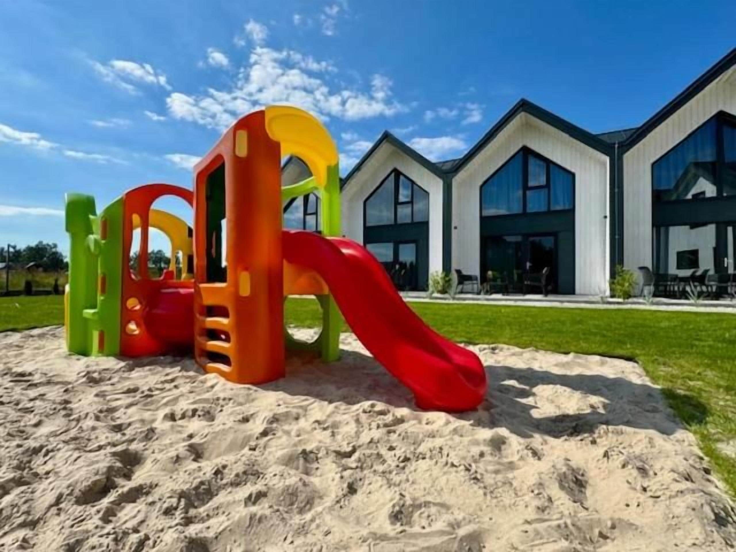 A playground with a red slide and climbing structures, located in front of a modern building with large windows.