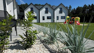 A modern two-story house with a paved driveway and a children's play area with colorful slides.