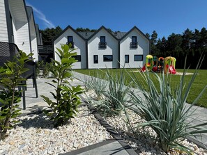 Una casa moderna de dos pisos con entrada pavimentada y un área de juegos infantiles con toboganes de colores.