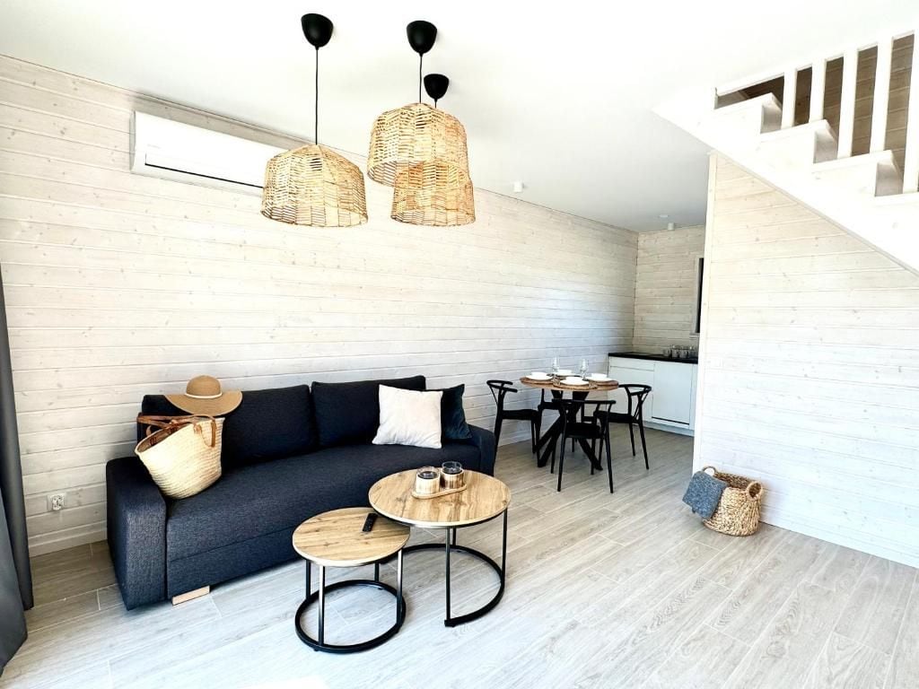 A modern living space with a sofa, two round tables, a dining area, and a staircase.