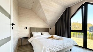 A bedroom with a large bed, a small side table, and a view of the outdoors through a large window. - Baltic Atelier (Grzybowo)