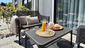 An outdoor seating area with a table set for breakfast, a sofa, and a glass partition. - Baltic Atelier (Grzybowo)