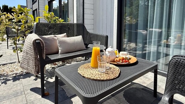 An outdoor seating area with a table set for breakfast, a sofa, and a glass partition. - Baltic Atelier (Grzybowo)