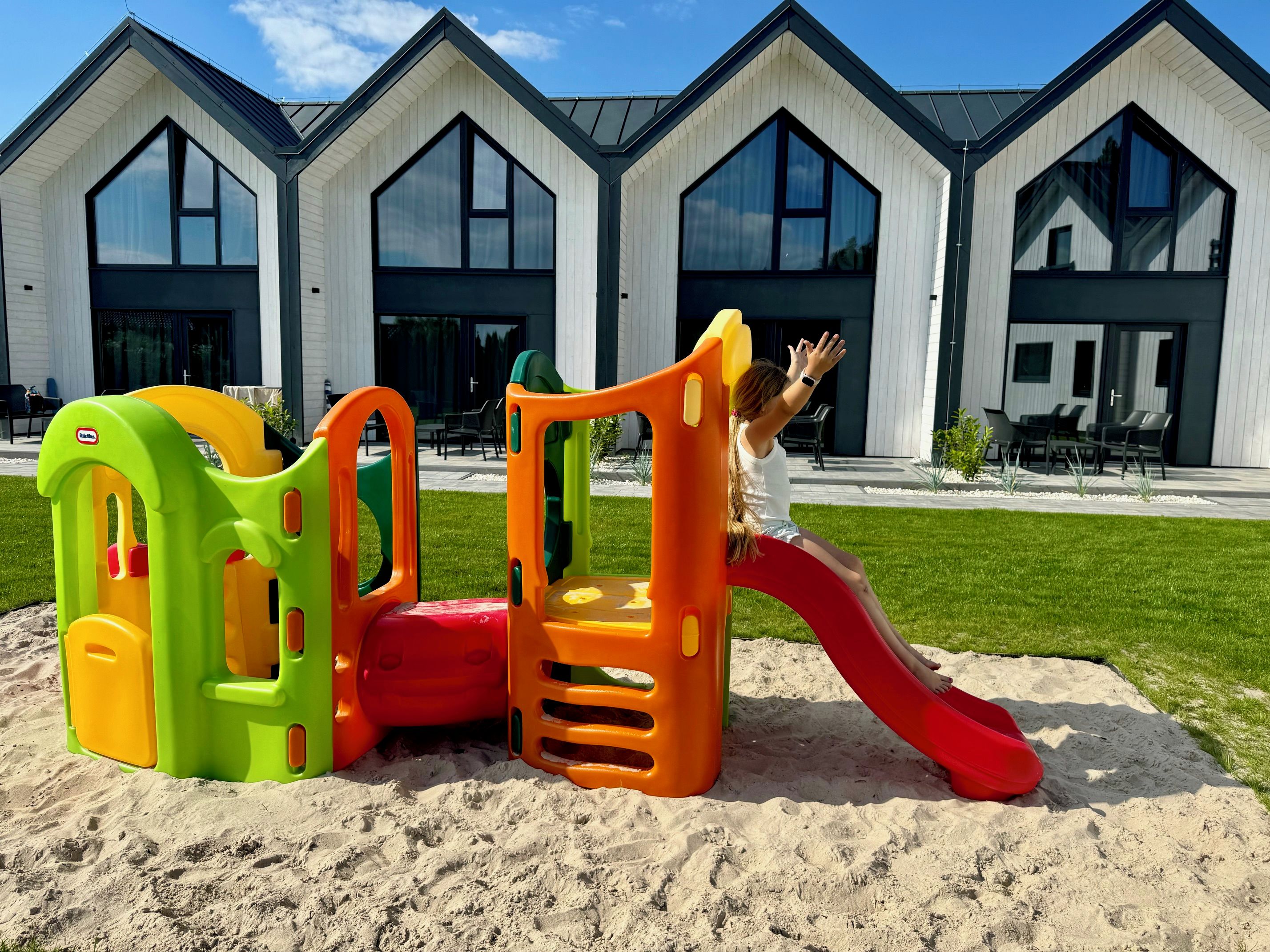 Un parque infantil con un tobogán y estructuras para escalar frente a un edificio con grandes ventanales.