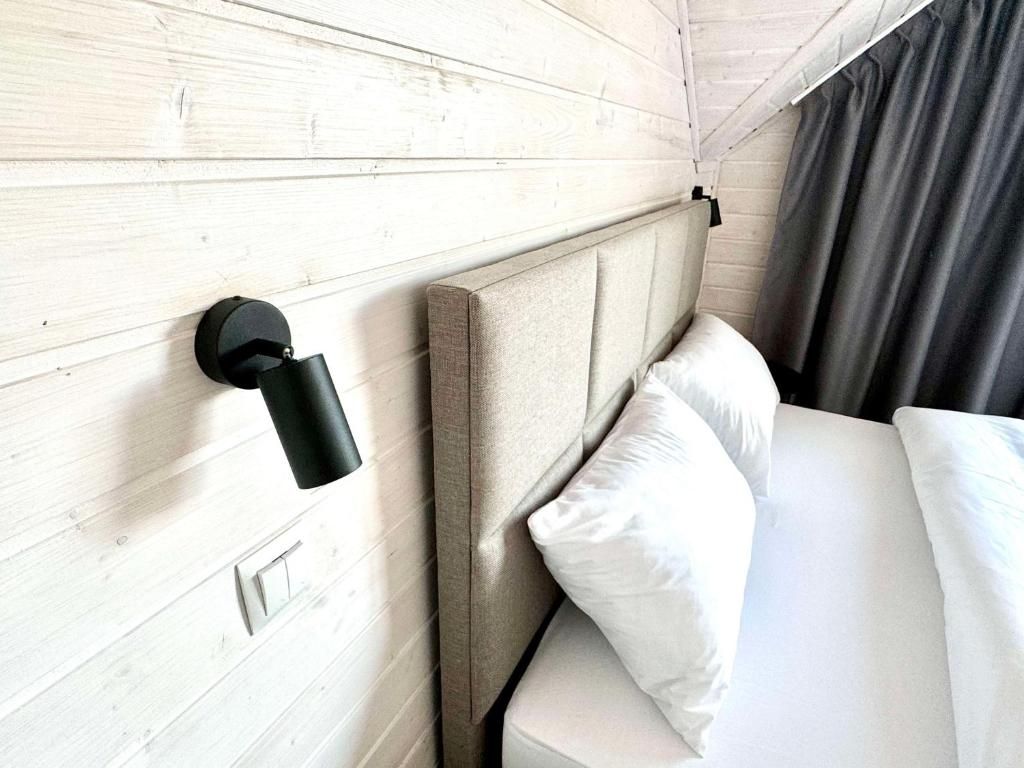 Ein Hotelzimmer mit einem Holz-Kopfteil, einer Wandleuchte, einem Bett mit weißer Bettwäsche und einem dunklen Vorhang.