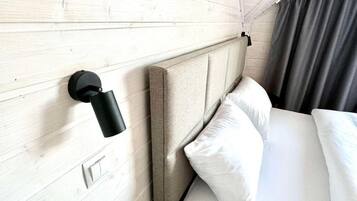 A hotel room with a wooden headboard, a wall-mounted light fixture, a bed with white bedding, and a dark curtain.
