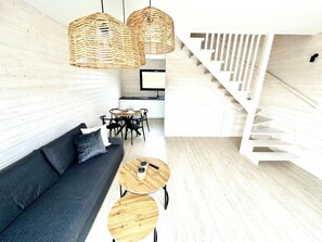 Un interior moderno con un sofá, mesas redondas de madera, lámparas colgantes de mimbre y una escalera.