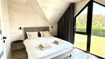 A bedroom with a large bed, a small table, and a window with a view of greenery.