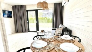 A dining area with a round table set for four, surrounded by black chairs, with a view of a house through a glass door. - Baltic Atelier (Grzybowo)