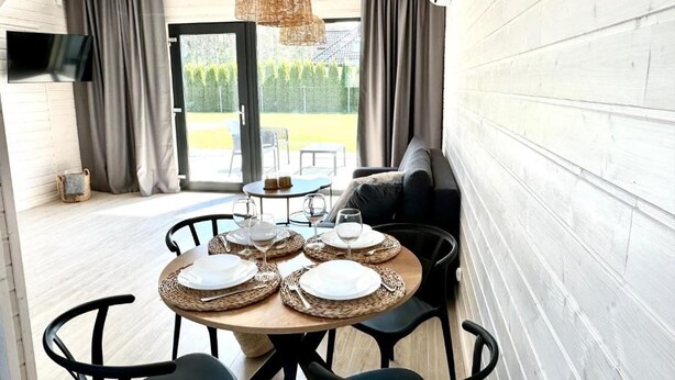 A dining area with a round table set for four, a sofa, and a television mounted on the wall. - Baltic Atelier (Grzybowo)