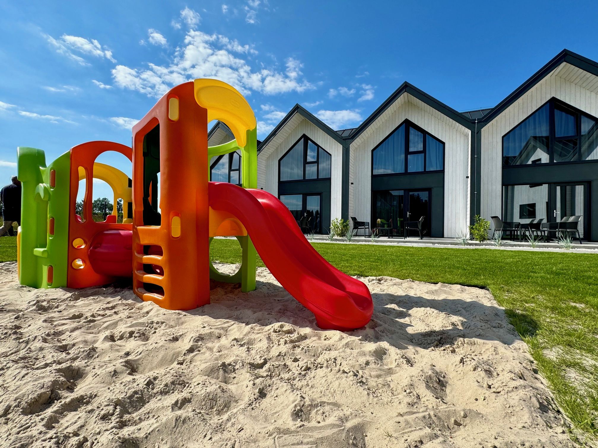 A playground with a slide and climbing structures, set against a modern building with large windows.