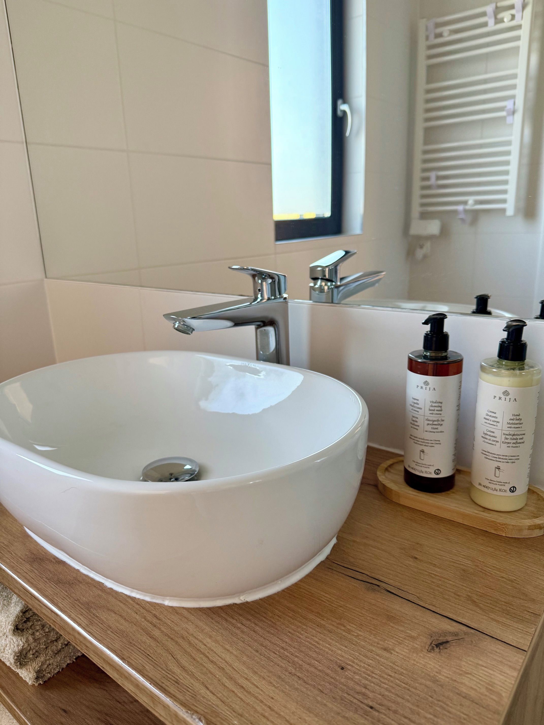 Un bagno con un lavandino bianco, un rubinetto cromato e due flaconi di lozione su un vassoio di legno.