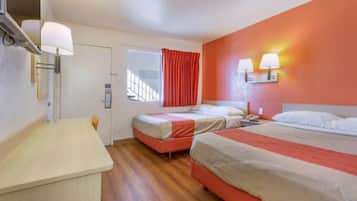 A hotel room with two beds, a desk, and a window with red curtains.