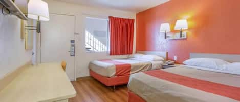 Een hotelkamer met twee bedden, een bureau en een raam met rode gordijnen.