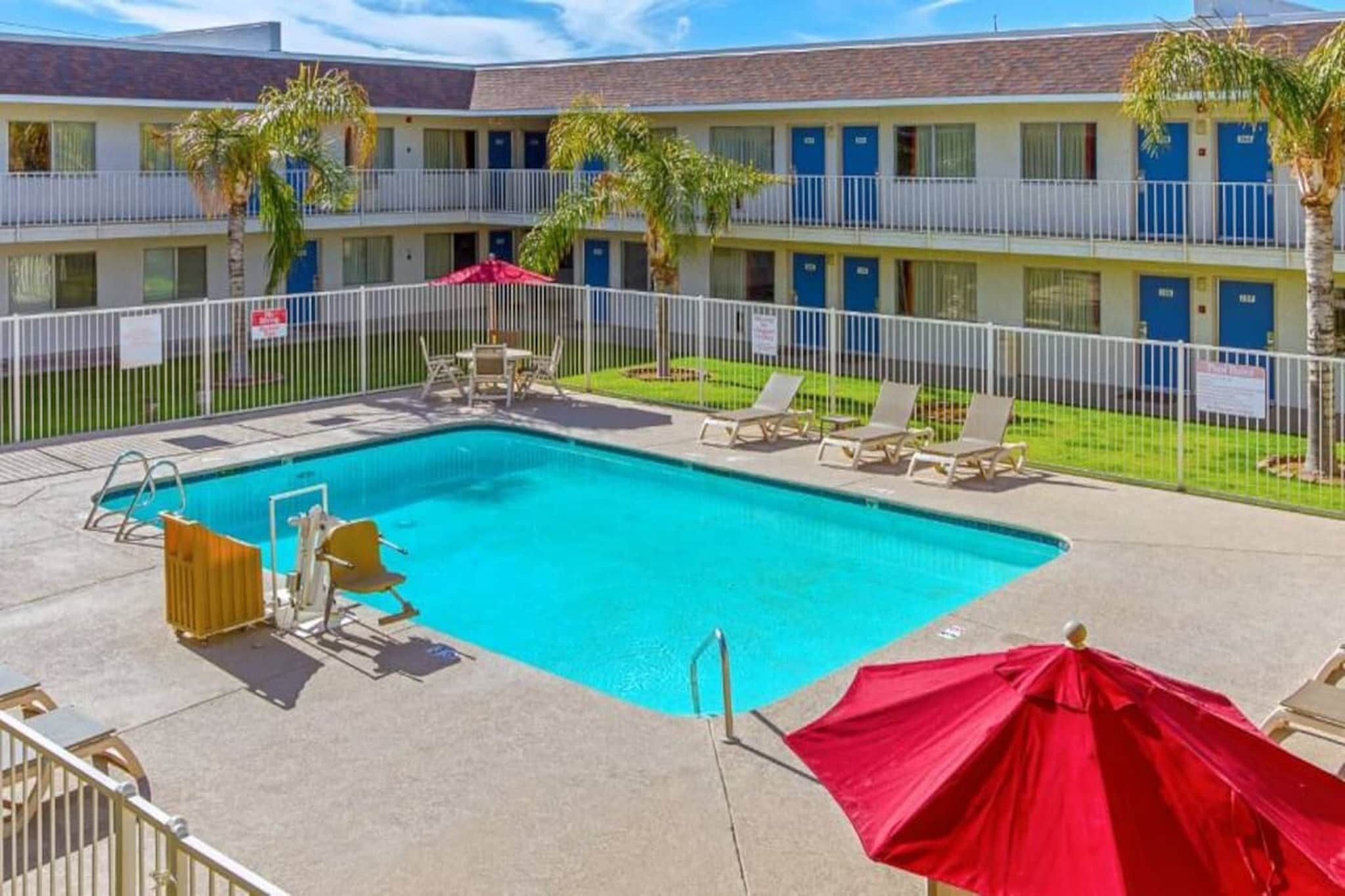 A hotel with a swimming pool, lounge chairs, and palm trees.