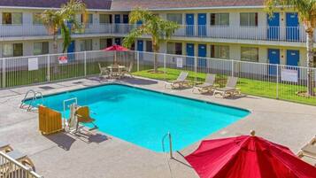 A hotel with a swimming pool, lounge chairs, and palm trees.
