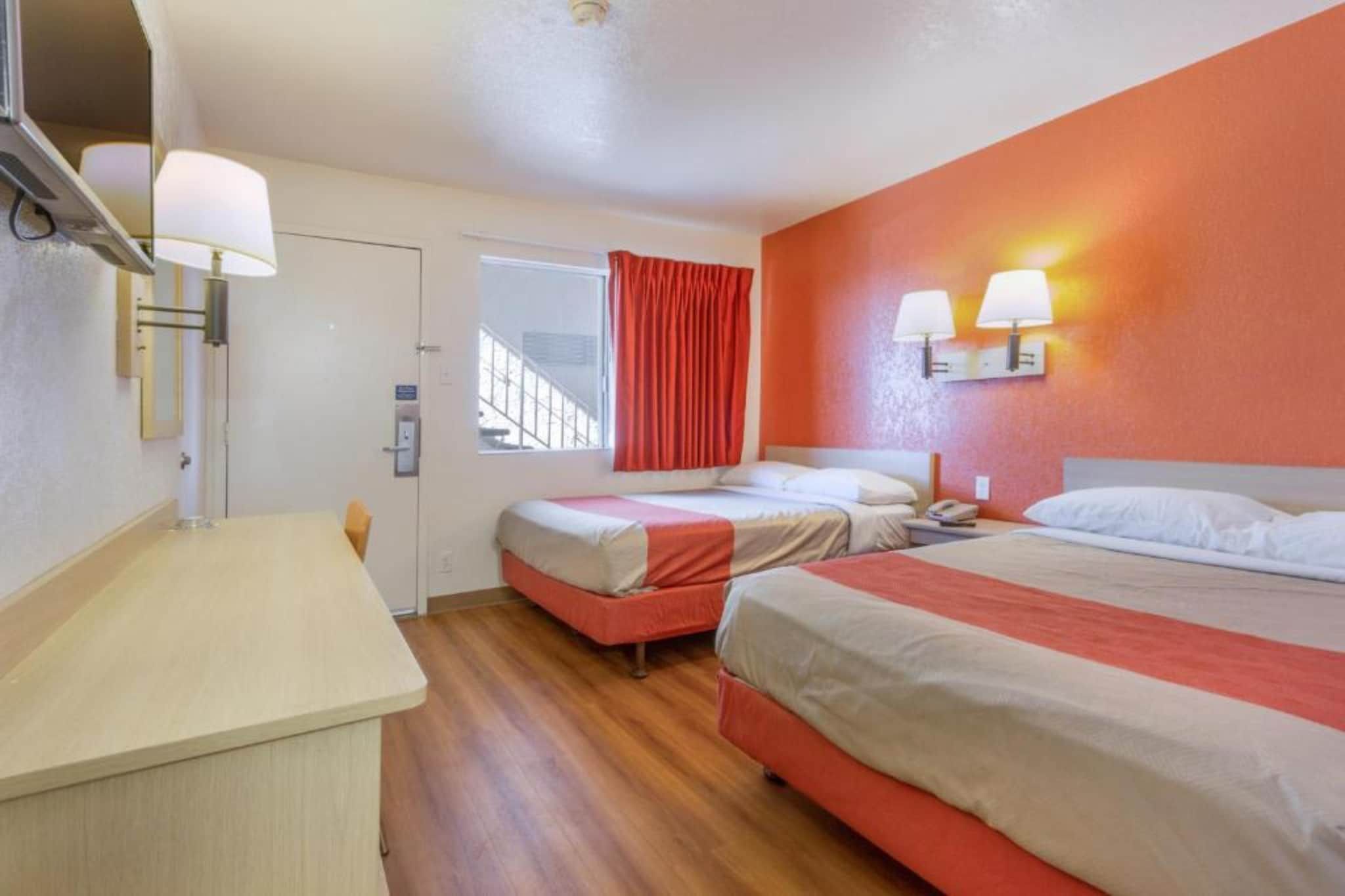 Ein Hotelzimmer mit zwei Betten, einem Schreibtisch, einem Fenster mit Vorhängen und Wandleuchten.