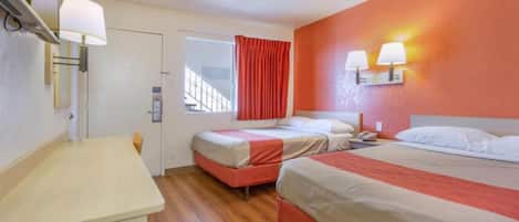 A hotel room with two beds, a desk, a window with curtains, and wall-mounted lamps.