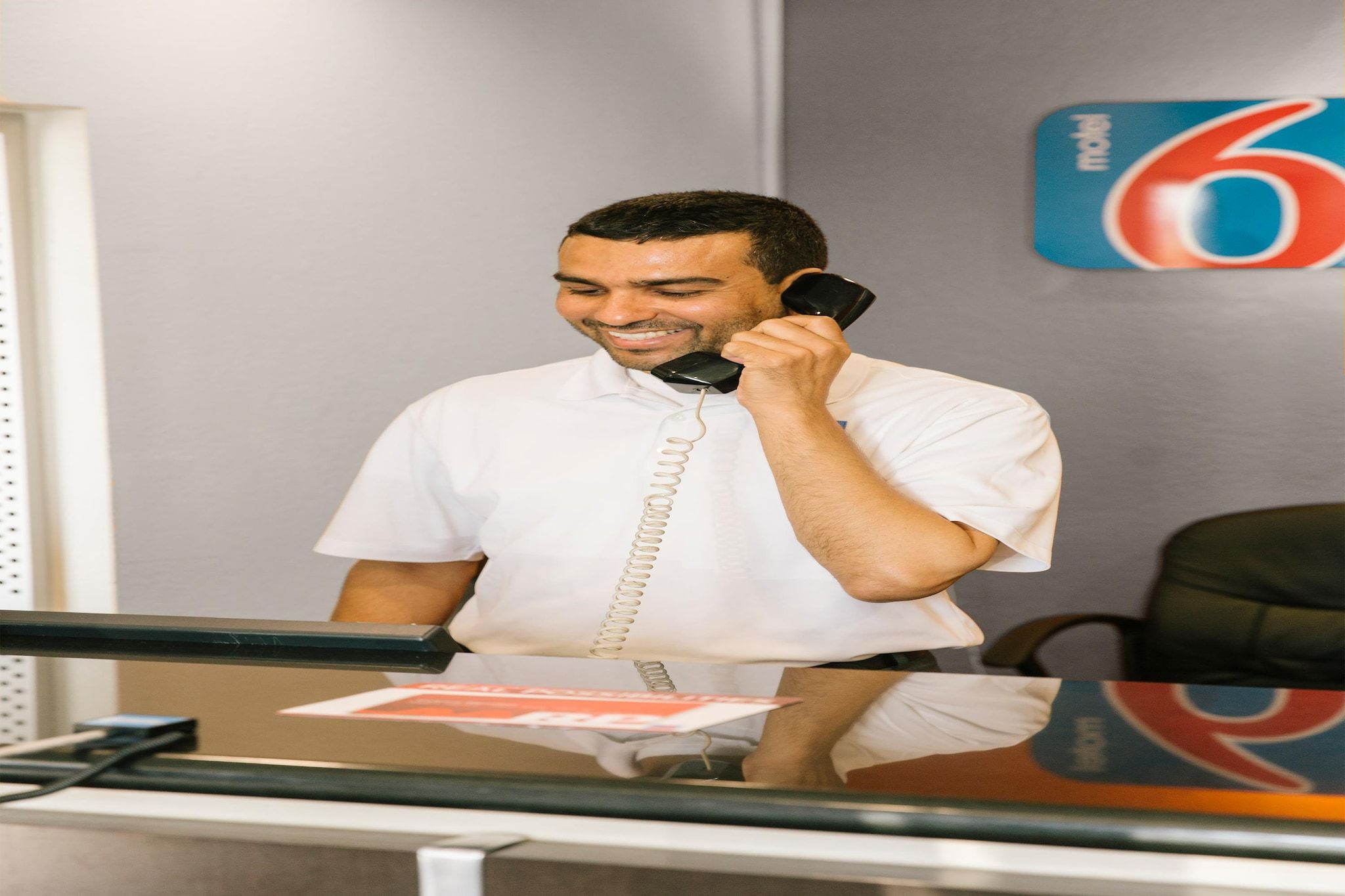 Eine Person am Schreibtisch mit Telefon, Notizbuch und einer Wand mit einem Hinweisschild.