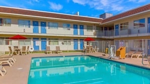 A pool area with lounge chairs and umbrellas, a multi-story building with balconies, and a clear blue sky. - 2 Full Beds | Premium (Phoenix)