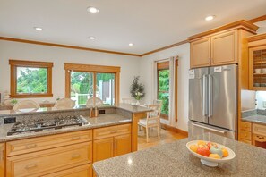 A kitchen with granite countertops, wooden cabinets, a stainless steel refrigerator, and a dining area with a table and chairs. - St Joseph River Retreat w/ Private Pool (Mishawaka)