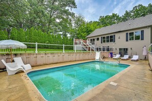 A rectangular swimming pool with a clear blue water surface, surrounded by a concrete deck. There are white lounge chairs and a white umbrella on the deck. A white fence encloses the deck area. - St Joseph River Retreat w/ Private Pool (Mishawaka)