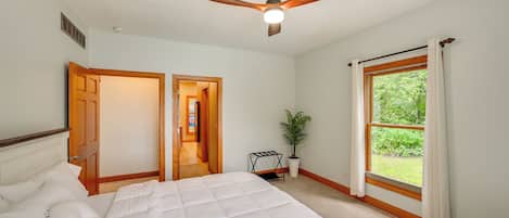 Quarto com cama, ventilador de teto, janela com cortinas e porta que dá para outro cômodo.
