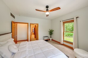 Ein Schlafzimmer mit einem Bett, einem Deckenventilator, einem Fenster mit Vorhängen und einer Tür zu einem anderen Raum.