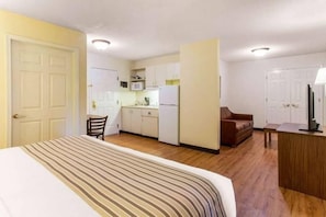 Ein kleines Hotelzimmer mit Bett, Küchenzeile, Sitzecke und Schreibtisch.