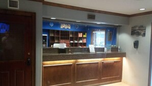 A reception desk with a blue backdrop, a wooden counter, and a tiled floor. - 1 Queen Bed | Mob Acc RI Shwr Nsmk Sofa (Myrtle Beach SC)