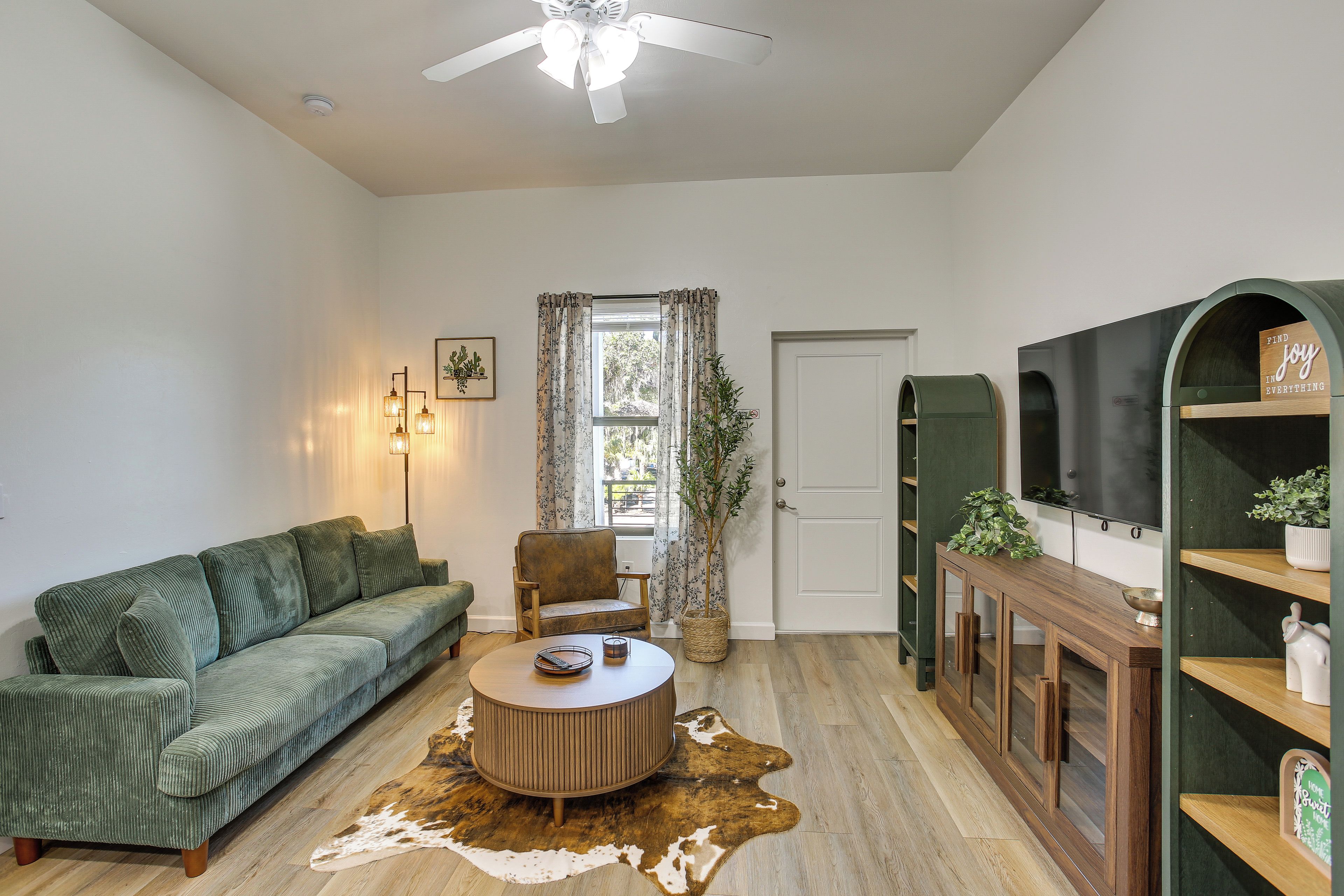 A living room with a green sofa, a round coffee table, a wooden cabinet, and a television on the wall.