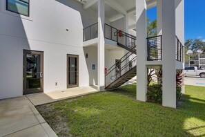 A building with a white exterior, a glass door entrance, and a metal staircase leading to an upper level. - Stylish Condo: Walk to Caloosahatchee River (LaBelle)
