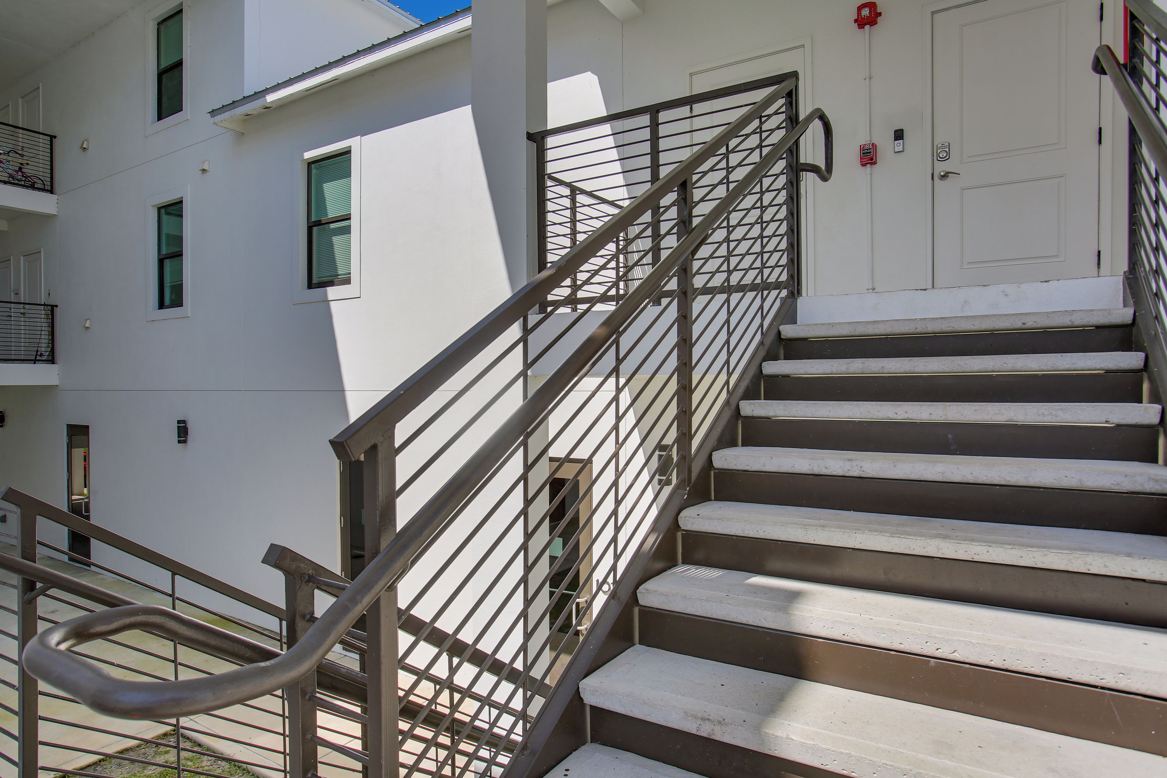 Escadas externas com grades de metal que levam à entrada de um edifício.