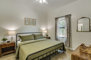 A bedroom with a bed, two bedside lamps, a nightstand, a mirror, and a window with curtains. - Stylish Condo: Walk to Caloosahatchee River (LaBelle)
