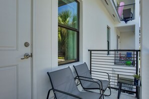 Ein Balkon mit Tisch und Stühlen, ein Fenster mit Blick auf Palmen und eine Tür.