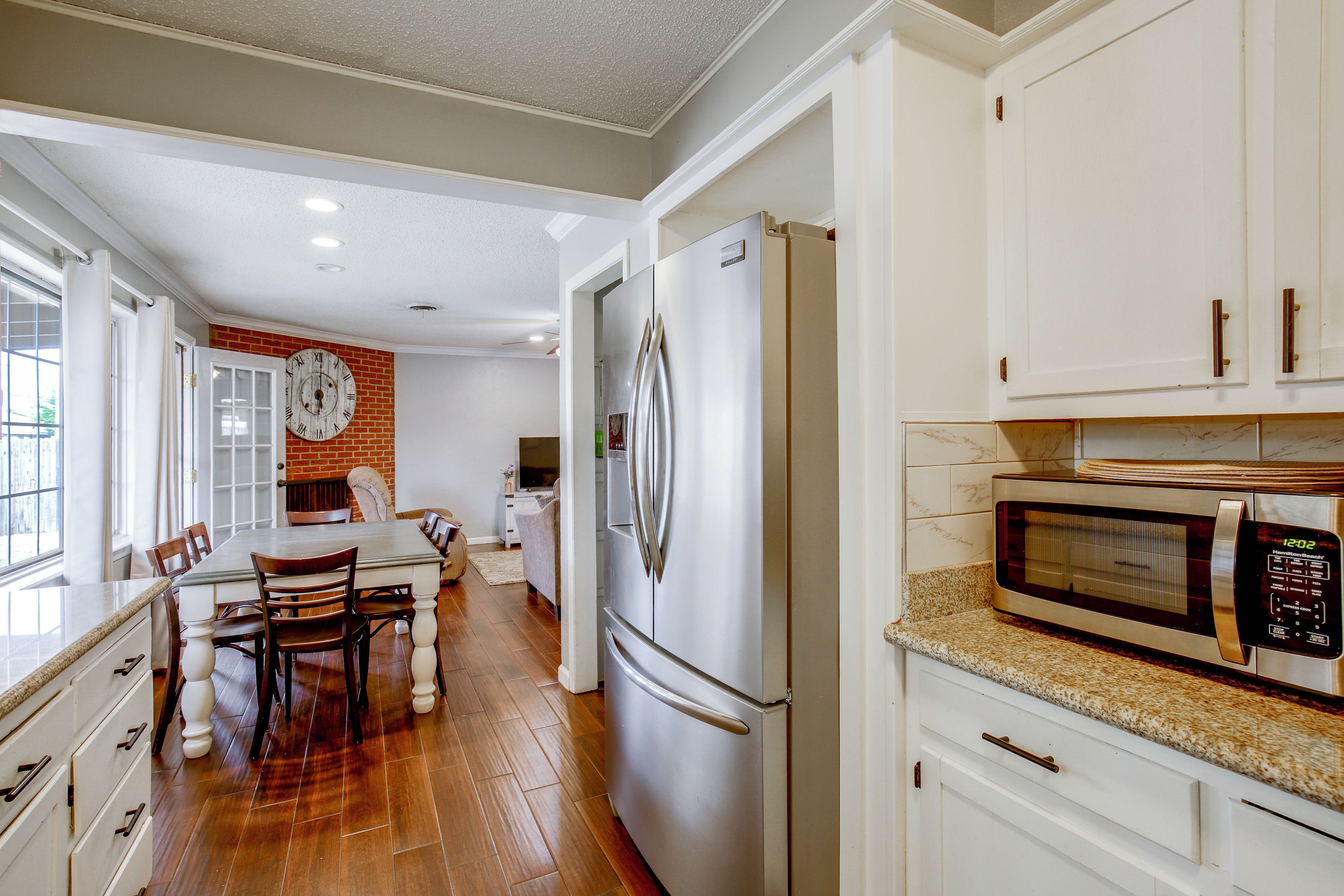 A kitchen with a refrigerator, microwave, and a clock on the wall.