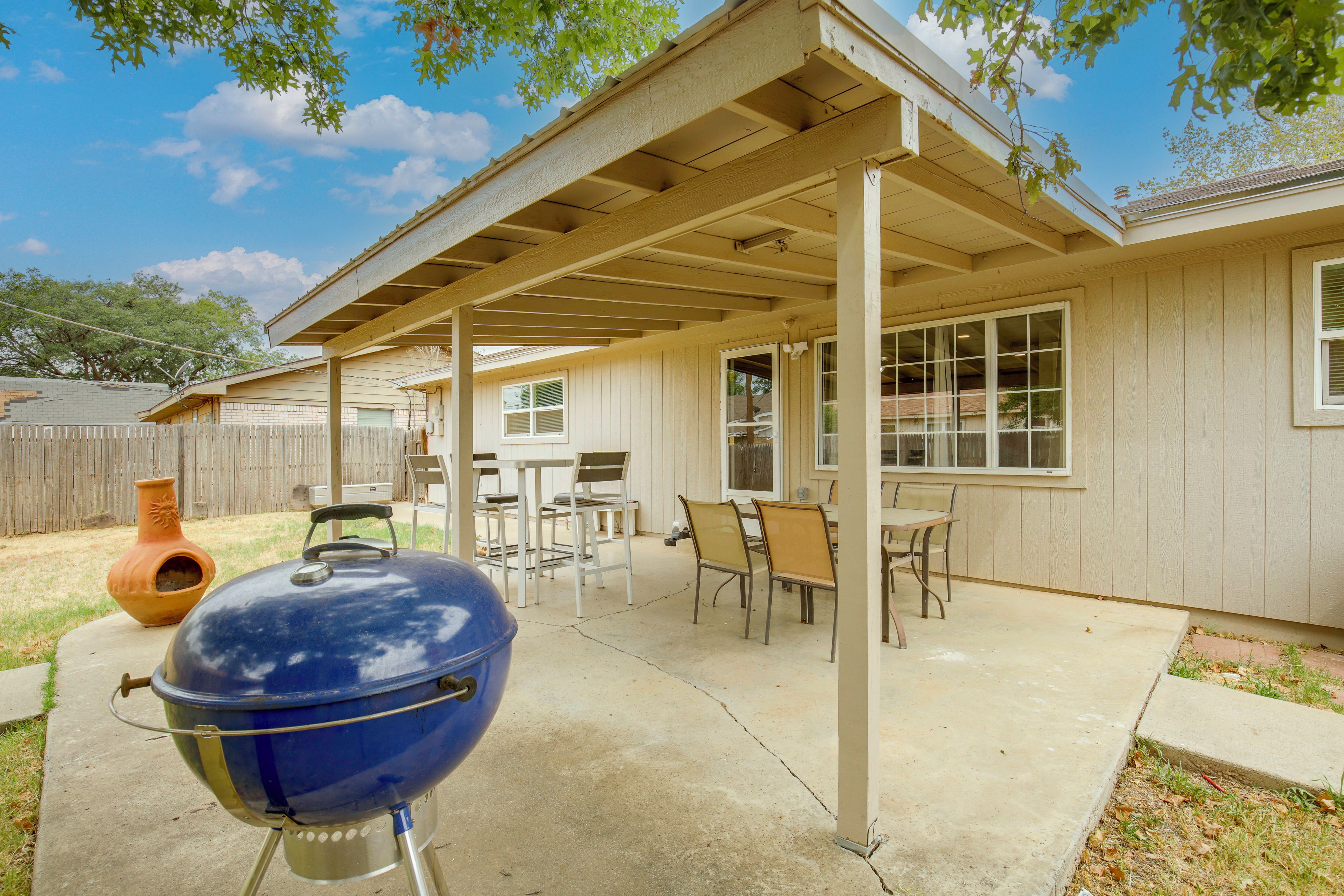 Ein überdachter Patio-Bereich mit Grill, Gartenmöbeln und Blick auf das Haus.