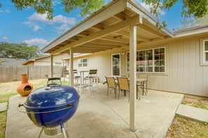Een overdekt terras met een barbecue, tuinmeubels en uitzicht op het huis.