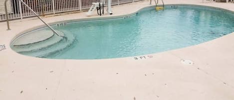 Una piscina con una marca de profundidad de 3 pies, un puesto de socorrista y un área vallada con sillas de descanso.