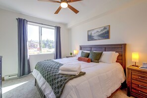 Une chambre avec un grand lit, un ventilateur de plafond, une fenêtre avec des rideaux, une table de chevet avec une lampe et un tableau au mur.