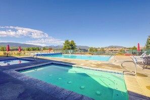 Une piscine avec plusieurs couloirs, entourée de chaises longues et de parasols, le tout sur fond de montagnes.