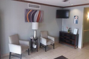 A waiting area with two patterned armchairs, a small table with a lamp, a television on the wall, and a wooden cabinet with a vase. - 1 King Bed | Non-Smoking, Micfridge (Myrtle Beach SC)