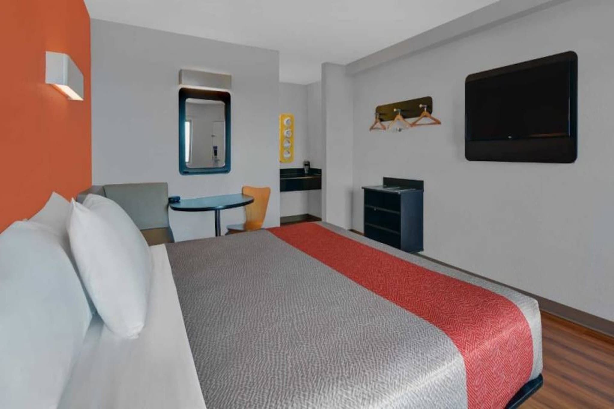 A hotel room with a bed, a desk, a chair, a small table, a mirror, a TV, and a wardrobe.