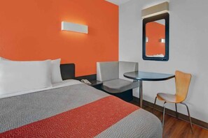 A hotel room with a bed, a desk, a chair, and a mirror.