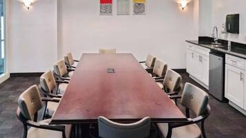 A conference room with a long table, chairs, and a kitchen area with cabinets and a microwave.